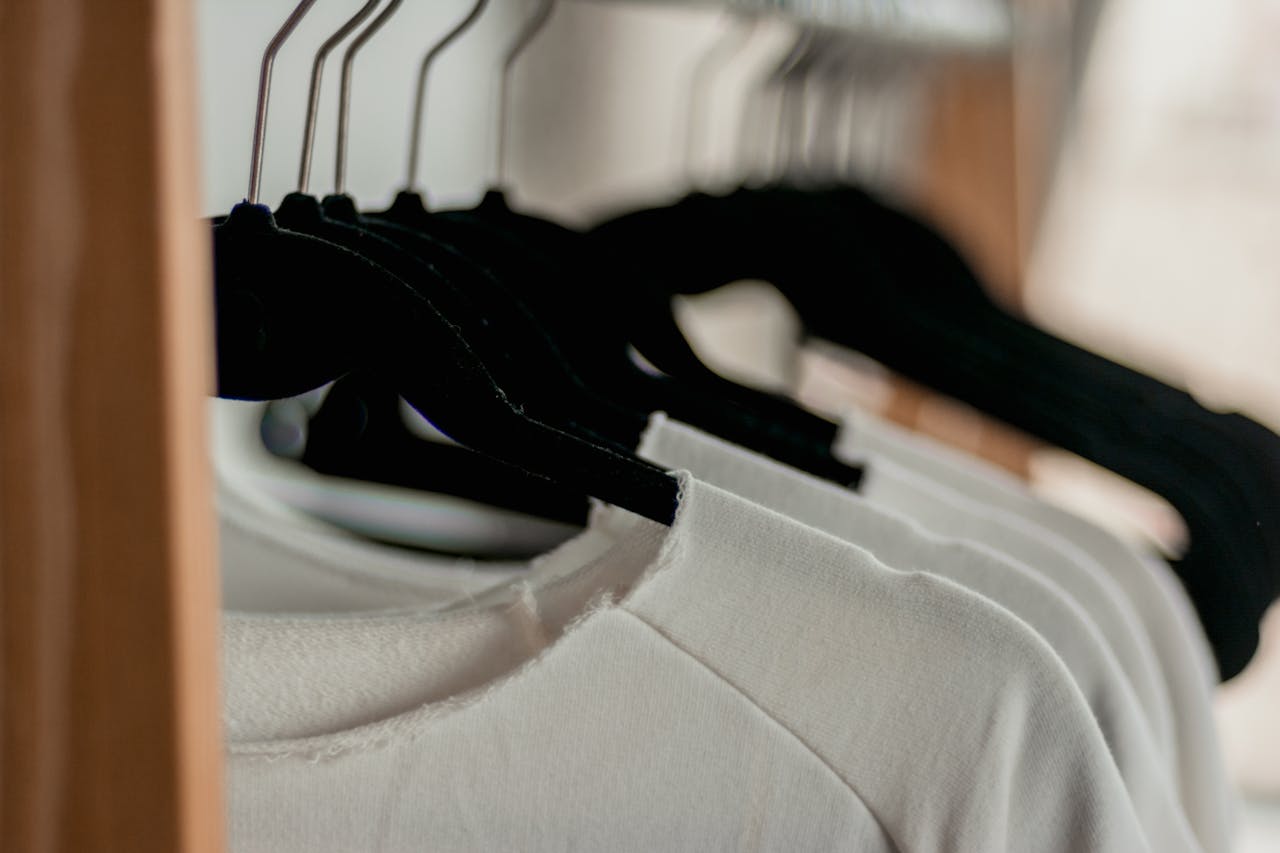 Close-up of white t-shirts hanging neatly on black hangers in a minimalist indoor closet setting.