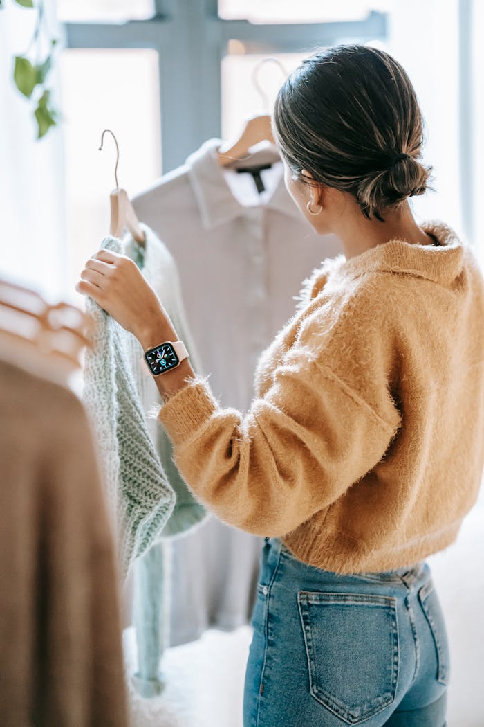 Back view of unrecognizable dark haired female in jeans choosing clothes near rack