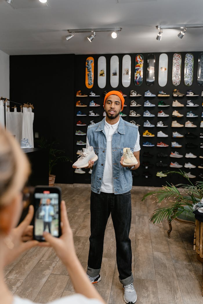 A man demonstrates shoes for an online promotional video in a boutique shop setting.